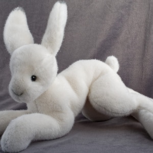 May include: A white plush bunny rabbit toy with long ears and a soft, fluffy texture. The bunny is lying on its side with its head turned to the side.