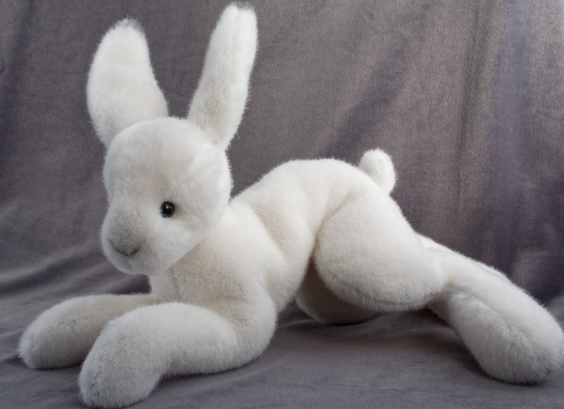 May include: A white plush bunny rabbit toy with long ears and a soft, fluffy texture. The bunny is lying on its side with its head turned to the side.