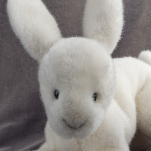 May include: A white plush bunny rabbit toy with long ears and a sweet expression. The bunny is lying down with its front paws extended.