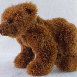 May include: A brown plush bear toy with a soft, furry texture. The bear is standing on all fours with its head turned to the side.