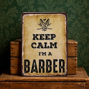 May include: A distressed metal sign with a brown frame and a tan background. The sign reads "KEEP CALM I'M A BARBER" in black, bold letters, with a barber pole and crossed razors graphic. The sign has a vintage aesthetic.