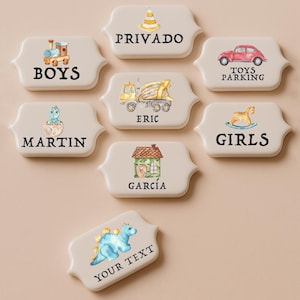May include: A collection of off-white ceramic plaques with watercolor illustrations and text. Designs include a train, car, dinosaur, and house. Text includes "BOYS", "TOYS PARKING", "GIRLS", "MARTIN", "ERIC", "GARCIA", "PRIVADO", and "YOUR TEXT".