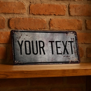 Puede incluir: Un letrero metálico rectangular con las palabras "YOUR TEXT" en letras negras en negrita. El letrero tiene un aspecto envejecido y vintage con un fondo gris y un borde marrón oxidado. Descansa sobre una estantería de madera contra una pared de ladrillo.
