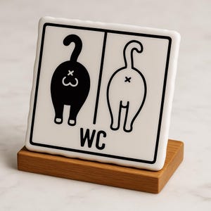 Op de afbeelding: Een wit vierkant bord met twee zwarte kattenbillen en de letters "WC" eronder. Het bord staat op een houten voet.
