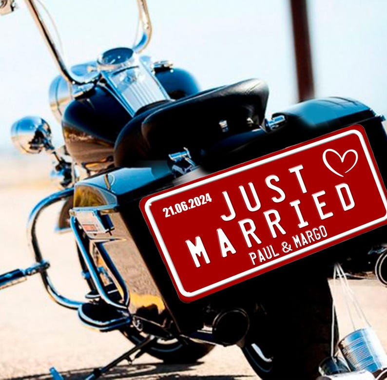 May include: A black motorcycle with chrome detailing. A red license plate on the rear displays "JUST MARRIED", a heart symbol, the date 21.06.2024, and the names Paul & Margo.