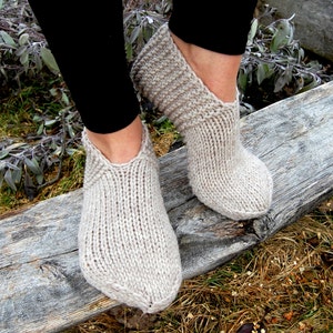 May include: A pair of beige knitted slipper socks with a pointed toe. The socks are made of a soft, warm material and are perfect for keeping your feet cosy.