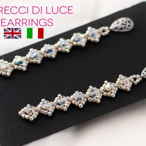 May include: A pair of silver earrings with a delicate, intricate design. Each earring features a row of clear crystals and a dangling teardrop-shaped charm.