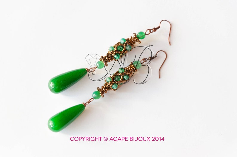 May include: A pair of long, green and gold earrings with teardrop-shaped green stones. The earrings are made with small beads and wire.