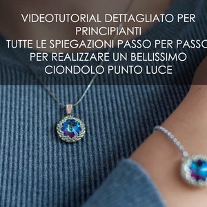 May include: A silver chain necklace with a blue and purple crystal pendant. The pendant is surrounded by a silver beaded border. The necklace is worn by a person with a blue sweater.