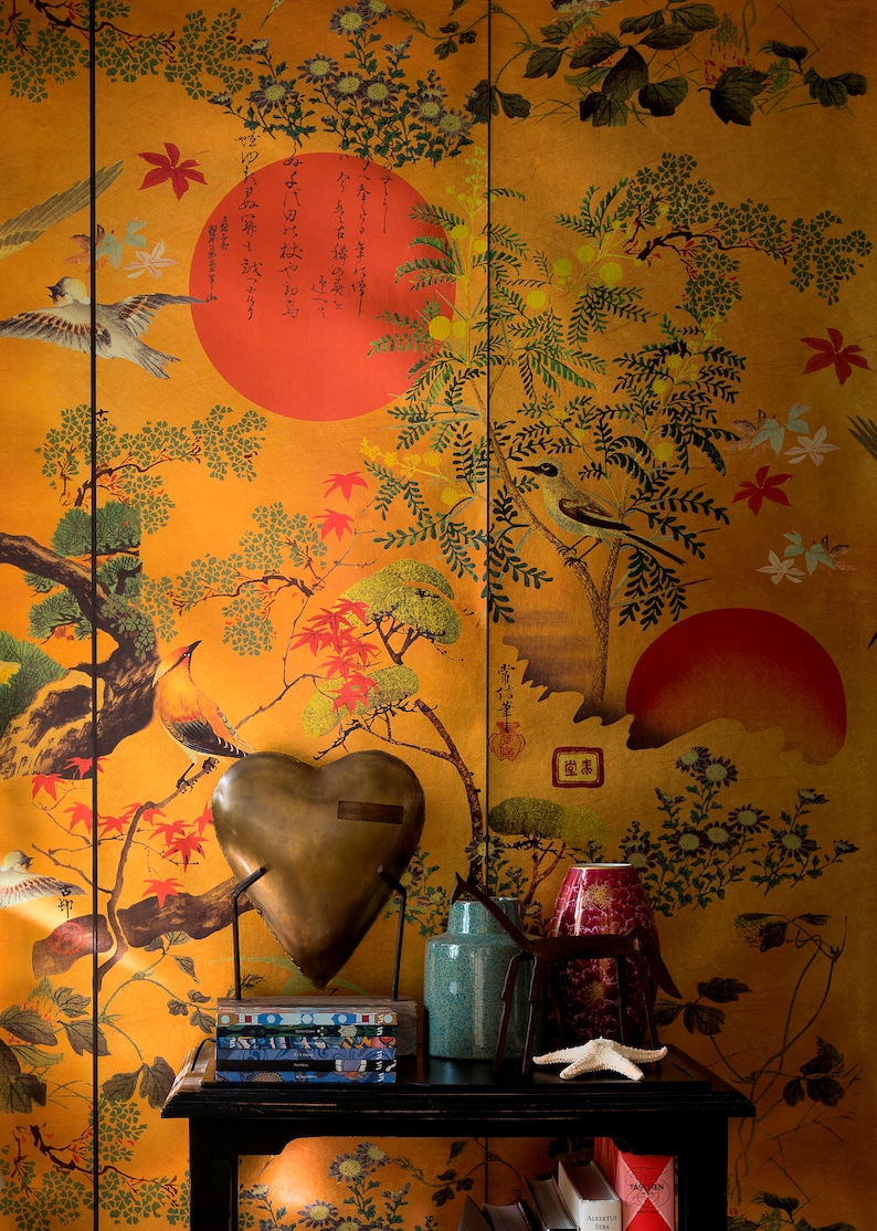 May include: A gold heart-shaped decorative object sits on a black table with a stack of books and a vase. The background is a gold wallpaper with a Japanese-inspired design featuring birds, trees, and flowers.