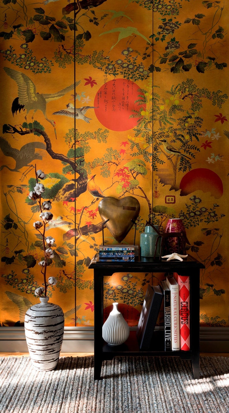 May include: A black end table with a white ceramic vase and a heart-shaped metal sculpture. The table is decorated with books and a small, white ceramic vase. The table is in front of a wall with a gold and red floral wallpaper with Japanese characters.