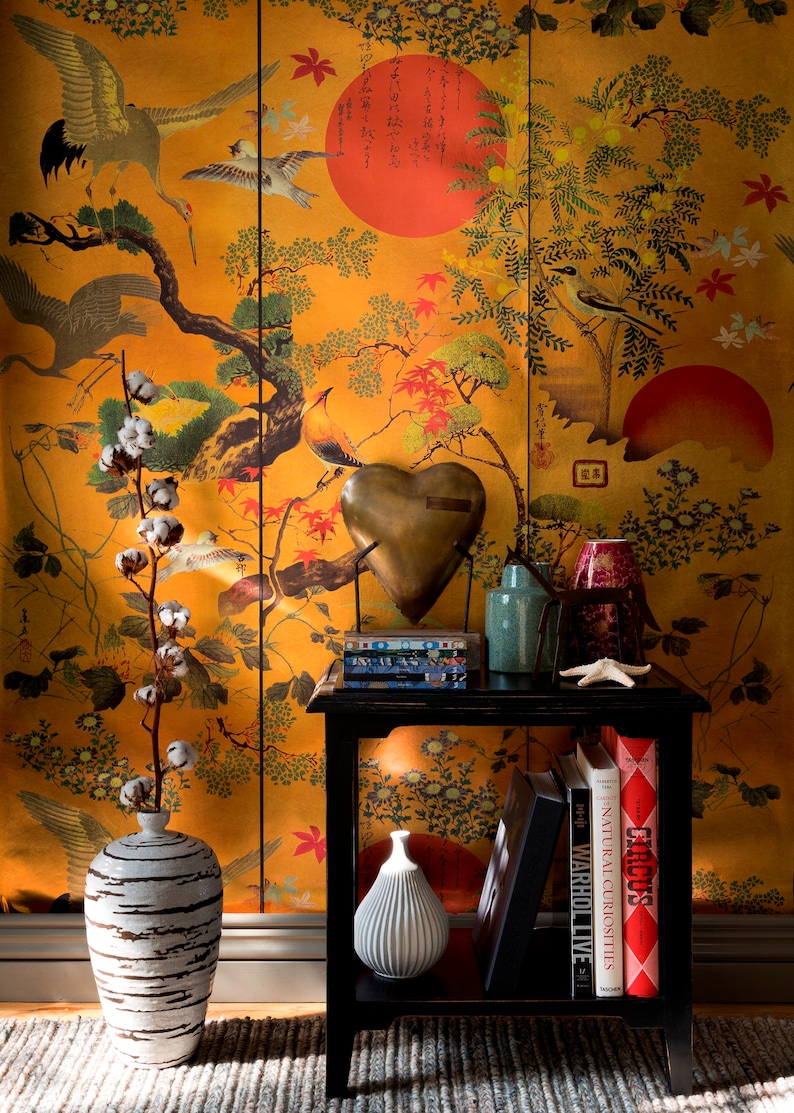 May include: A black end table with a gold heart-shaped sculpture, two vases, and a stack of books. The table is in front of a wall with a Japanese-style wallpaper featuring birds, flowers, and a red sun.