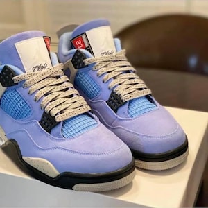 Puede incluir: Un par de zapatillas de gamuza azul claro con detalles negros y cordones blancos. Las zapatillas tienen una entresuela blanca y una suela negra. El texto "Flight" es visible en el lateral de la zapatilla izquierda.