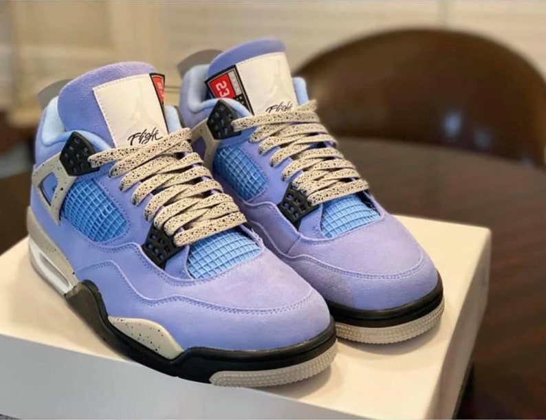 Puede incluir: Un par de zapatillas de gamuza azul claro con detalles negros y cordones blancos. Las zapatillas tienen una entresuela blanca y una suela negra. El texto "Flight" es visible en el lateral de la zapatilla izquierda.