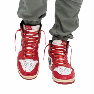 May include: A pair of red and white high-top sneakers with black Nike Air branding on the side and tongue. The laces are red and the shoes are worn.