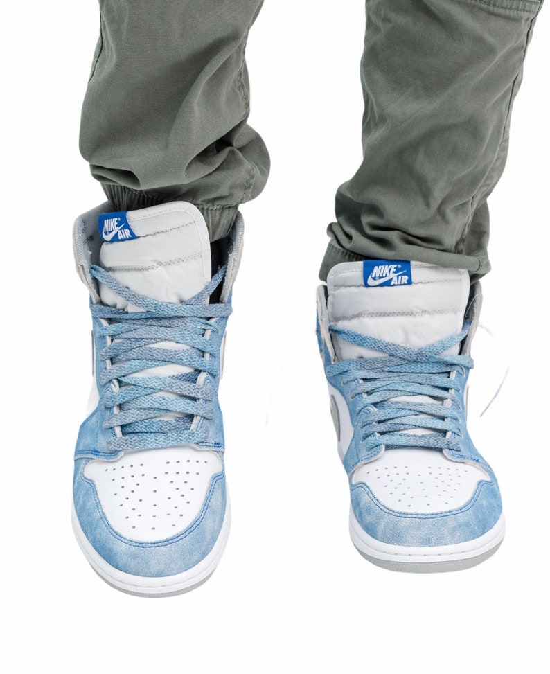 May include: A pair of light blue and white sneakers with a white swoosh and the text "Nike Air" on the side. The sneakers are worn by a person wearing grey pants.