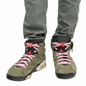 May include: A pair of olive green high-top sneakers with pink laces and orange accents. The sneakers are worn by a person wearing olive green pants.