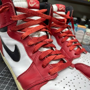 May include: Pair of red, white, and black high-top sneakers with red laces. The sneakers feature a black Nike swoosh on the side and the Nike Air logo on the tongue. The shoes have a worn, vintage look.