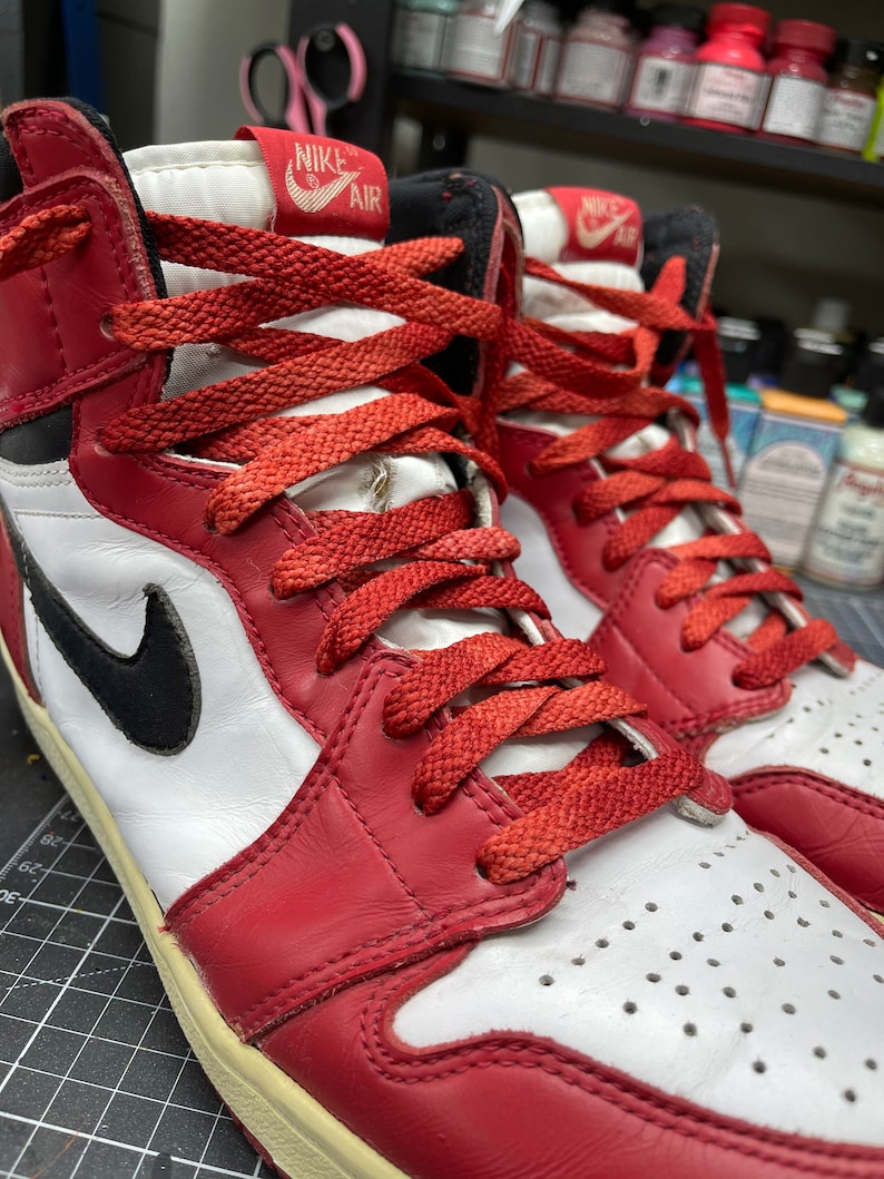 May include: Pair of red, white, and black high-top sneakers with red laces. The sneakers feature a black Nike swoosh on the side and the Nike Air logo on the tongue. The shoes have a worn, vintage look.