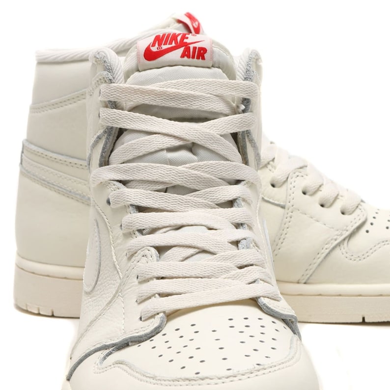 May include: A pair of off-white high-top sneakers with a white laces and a red "Nike Air" logo on the tongue.
