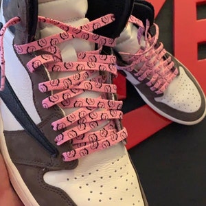 Puede incluir: Zapatillas altas con paneles blancos, marrones y negros. Los zapatos tienen cordones rosas con un gr&aacute;fico negro repetido. El logotipo de Nike Air es visible en la leng&uuml;eta.