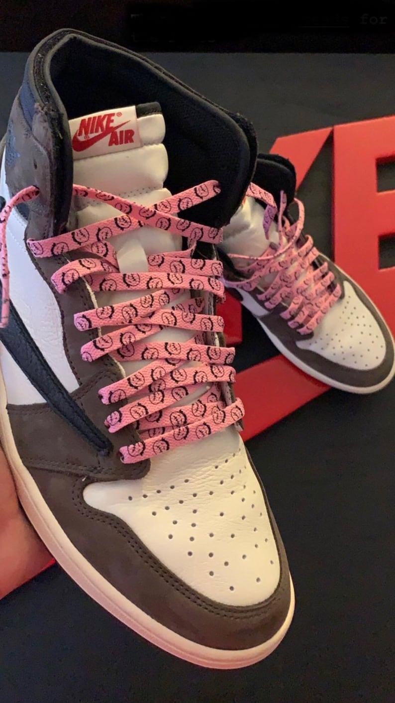 Puede incluir: Zapatillas altas con paneles blancos, marrones y negros. Los zapatos tienen cordones rosas con un gr&aacute;fico negro repetido. El logotipo de Nike Air es visible en la leng&uuml;eta.