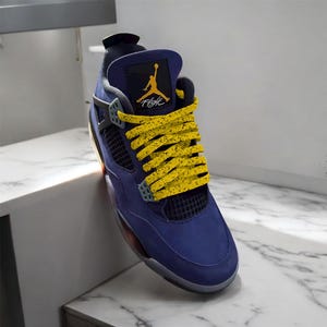 May include: A single blue and gray athletic shoe with yellow speckled laces. The shoe features a yellow Jumpman logo and the word "Flight". The shoe is angled on a white surface.