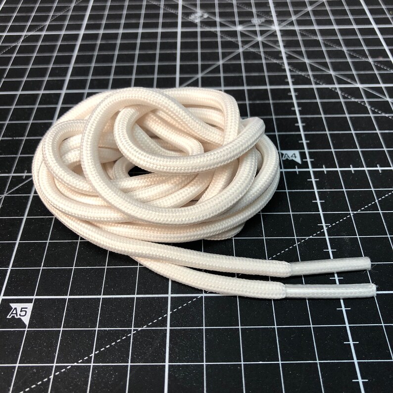 Puede incluir: Un par de cordones blancos, enrollados y dispuestos sobre una superficie de rejilla negra.