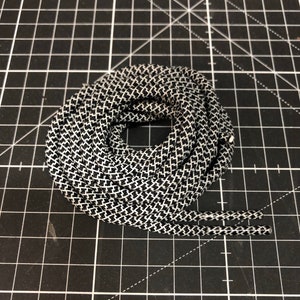 Puede incluir: Primer plano de un cord&oacute;n de zapato con estampado en blanco y negro. El cord&oacute;n est&aacute; enrollado y los extremos son visibles.
