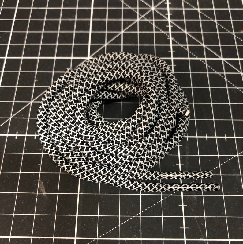 Puede incluir: Primer plano de un cord&oacute;n de zapato con estampado en blanco y negro. El cord&oacute;n est&aacute; enrollado y los extremos son visibles.