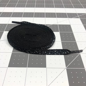 Puede incluir: Cordones negros con motas blancas. Los cordones est&aacute;n enrollados y los extremos son visibles.