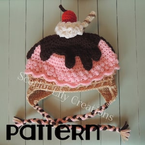 Puede incluir: Gorro de helado de ganchillo en rosa, marrón y beige. El gorro tiene una cereza, crema batida blanca y salsa de chocolate. Tiene lazos trenzados en las orejeras. La palabra "PATTERN" está en la parte inferior.