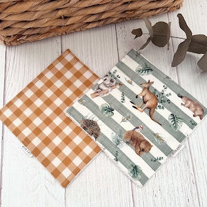 May include: Two square baby bibs. One is a tan and white gingham pattern. The other has a white background with green stripes and illustrations of Australian animals, including a koala, kangaroo, and platypus.