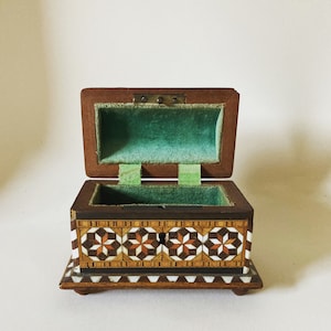 May include: An open wooden box with a green velvet interior. The box is decorated with a geometric pattern of wood and mother of pearl.