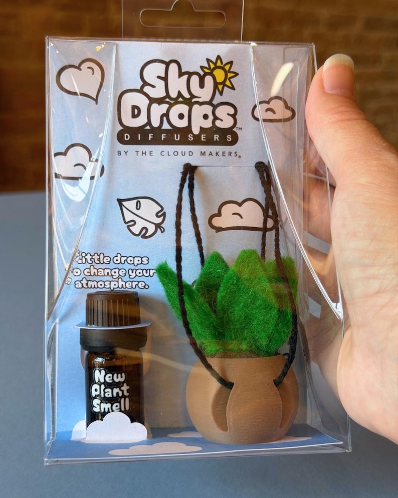 May include: A Sky Drops Diffuser kit in clear plastic packaging containing a small brown glass bottle labeled New Plant Smell and a miniature green felt plant in a tan pot with black hanging strings. The packaging features clouds and text.