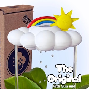 K&ouml;nnte beinhalten: Ein wei&szlig;es, wolkenf&ouml;rmiges Bew&auml;sserungsger&auml;t f&uuml;r Pflanzen mit einer gelben Sonne und einem bunten Regenbogen. Das Ger&auml;t hat klare vertikale St&uuml;tzen und h&auml;ngende Tropfen. Die Verpackung zeigt den Text "The Original with Sun and Rainbow Charms".