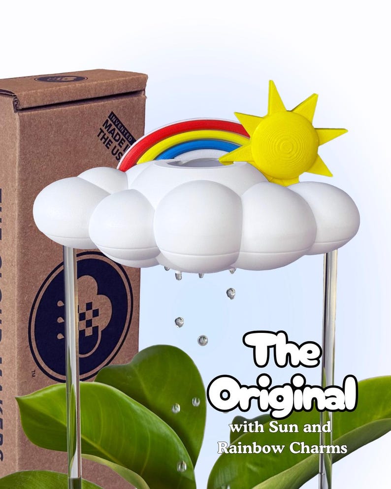 K&ouml;nnte beinhalten: Ein wei&szlig;es, wolkenf&ouml;rmiges Bew&auml;sserungsger&auml;t f&uuml;r Pflanzen mit einer gelben Sonne und einem bunten Regenbogen. Das Ger&auml;t hat klare vertikale St&uuml;tzen und h&auml;ngende Tropfen. Die Verpackung zeigt den Text "The Original with Sun and Rainbow Charms".