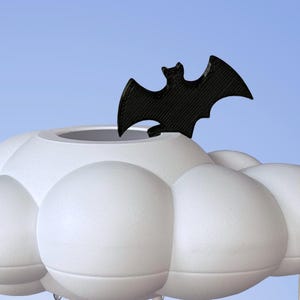 May include: A white cloud-shaped planter with a black bat figurine perched on top. The planter has a rounded, puffy design.