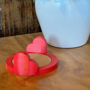 以下が含まれることがあります： コルクの中心を持つ赤いハート型のコースター。コースターは3Dプリントされたプラスチック製で、滑らかで光沢のある仕上げになっています。
