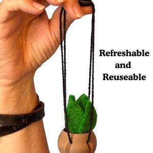 May include: A small green felt plant in a tan spherical pot suspended by thin black cords. The text "Refreshable and Reuseable" is printed to the right. The pot features a smooth, rounded base with integrated slots for the hanging cords.