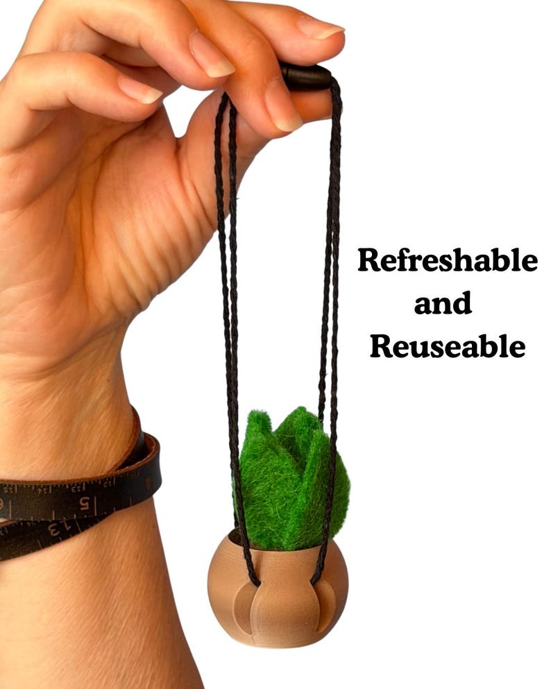 May include: A small green felt plant in a tan spherical pot suspended by thin black cords. The text "Refreshable and Reuseable" is printed to the right. The pot features a smooth, rounded base with integrated slots for the hanging cords.
