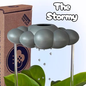 May include: A gray cloud-shaped plant mister with clear support rods, simulating rain. The text "The Stormy" is above the mister. A cardboard box with "Invented & Made in the USA" is in the background. Green leaves are in the foreground.