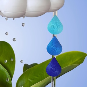 May include: A white cloud with raindrops falling from it. Three teardrop-shaped ornaments hang from a metal rod, each a different shade of blue, from light blue to dark blue.