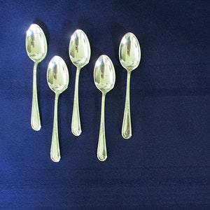 May include: Five silver teaspoons arranged in a row on a dark blue tablecloth.