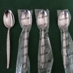 Può includere: Un set di quattro cucchiai in acciaio inossidabile, tre ancora nella loro confezione di plastica originale. I cucchiai hanno un manico strutturato e una superficie lucida. Per l'uso a tavola.