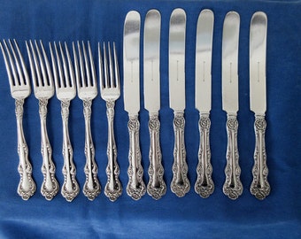 Puede incluir: Un juego de diez cubiertos de plata plateada, que incluye ocho tenedores y dos cuchillos para mantequilla. Los tenedores tienen mangos ornamentados con un diseño floral. Los cuchillos tienen un diseño similar en los mangos y son ligeramente más largos que los tenedores.