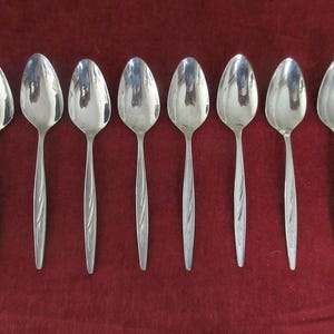 Puede incluir: Ocho cucharas de plata con un diseño retorcido en el mango. Las cucharas están dispuestas en una fila sobre una superficie roja.