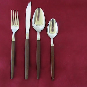 Könnte beinhalten: Ein vierteiliges Besteckset bestehend aus einer Gabel, einem Messer, einem großen Löffel und einem kleinen Löffel. Jedes Teil hat einen Kopf aus poliertem, silberfarbenem Metall und einen geraden, dunkelbraunen Griff mit matter Oberfläche.
