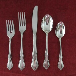 May include: Five pieces of silverware, including a knife, fork, and three spoons, all with ornate handles and a polished silver finish.