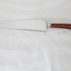 May include: A silver cake server with a serrated edge and a brown wood handle.